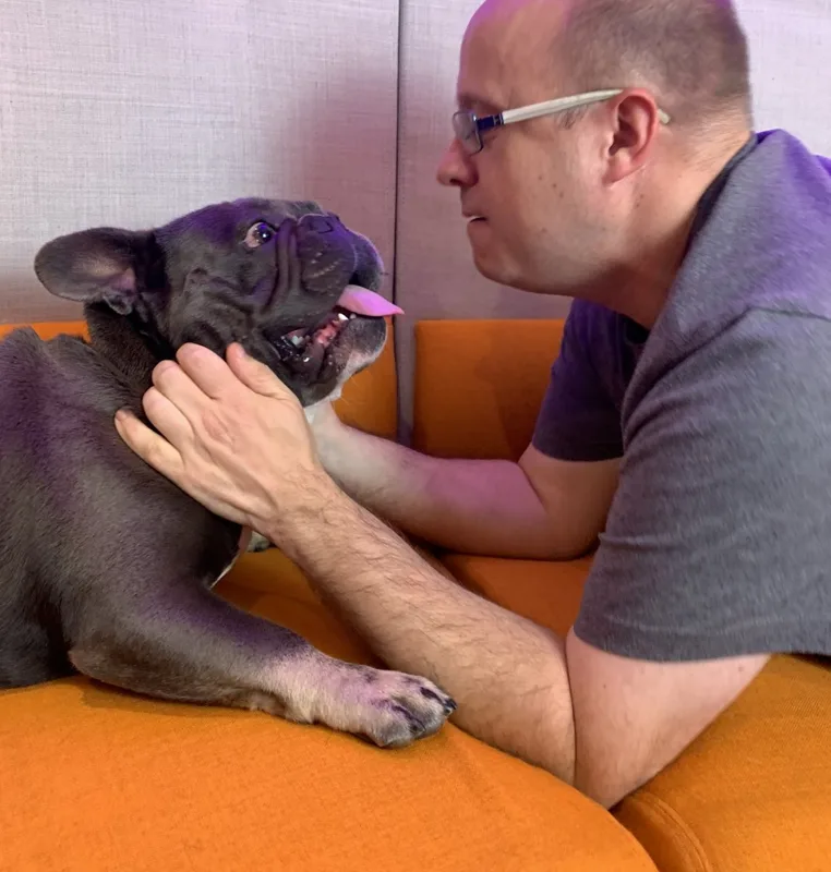 Jonathan face to face with Dembe, his French bulldog, on an orange sofa